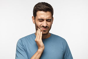 Young man holding jaw in pain from tooth ache before receiving tooth extraction from Mountain State Oral and Facial Surgery in Hurricane, WV Young man holding jaw in pain from tooth ache before receiving tooth extraction from Mountain State Oral and Facial Surgery in Hurricane, WV