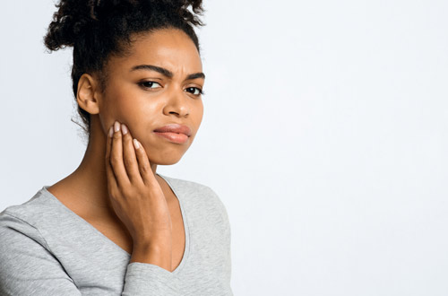 Black female patient holding jaw from tooth pain before tooth extraction at Mountain State Oral and Facial Surgery in Princeton, WV
