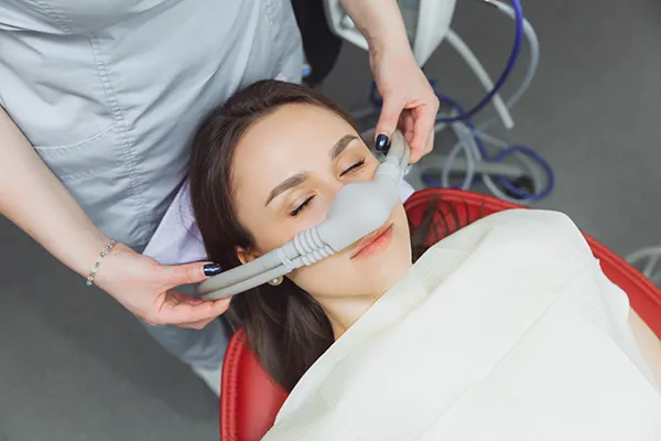 Dental assistant fitting a sedation mask over the nose of her calm female patient before tooth extraction at Mountain State Oral and Facial Surgery in Ashland, KY Dental assistant fitting a sedation mask over the nose of her calm female patient before tooth extraction at Mountain State Oral and Facial Surgery in Ashland, KY