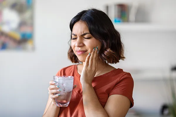 Young woman rubbing her jaw and wincing from wisdom teeth pain before removal at Mountain State Oral and Facial Surgery in Hurricane, WV