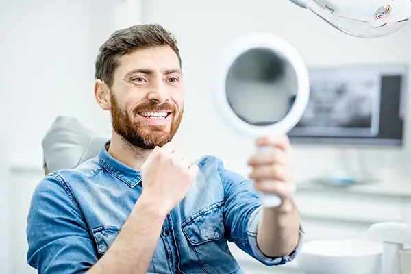 Bearded patient checking out his handsome smile with dental implants in a mirror while sitting in a dental chair from Mountain State Oral and Facial Surgery in Beckley, WV Bearded patient checking out his handsome smile with dental implants in a mirror while sitting in a dental chair from Mountain State Oral and Facial Surgery in Beckley, WV