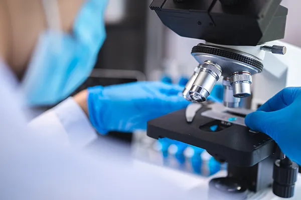 Over-the-shoulder look at a specialist using a microscope to investigate a dental biopsy.